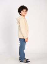 Child wearing a beige hoodie and blue jeans on a white background