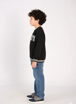 Child wearing a black sweatshirt with text and blue jeans on a white background