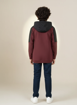 Person wearing a maroon and black hoodie with navy pants on a beige background