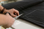Person cutting black fabric with scissors on a white surface