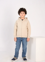 Child wearing a beige hoodie and blue jeans on a white background