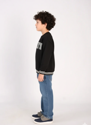 Child wearing a black sweatshirt with text and blue jeans on a white background