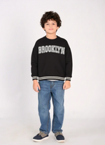 Child wearing a black sweatshirt with 'Brooklyn' text on a white background