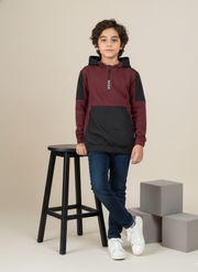 Child wearing a maroon and black hoodie standing next to a stool and blocks on a beige background